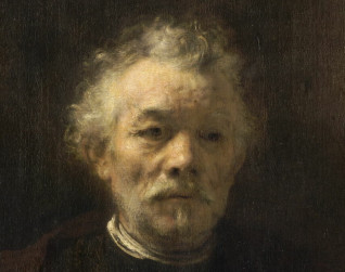 Portret starszego mężczyzny z krótkimi, kręconymi siwymi włosami, przystrzyżoną brodą i wąsami. Ubrany w brązowy płaszcz z kołnierzem i białą koszulę. Tło jest ciemne i neutralne.