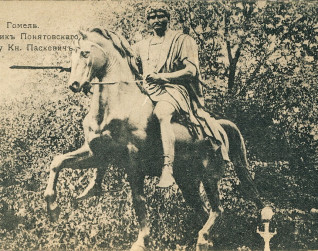 Pomnik konny Józefa Poniatowskiego w Homlu, przedstawiający jeźdźca w klasycznym stroju na wspiętym koniu. W tle drzewa. Widoczny napis w cyrylicy.