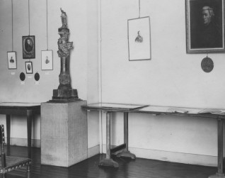 Wnętrze Muzeum Adama Mickiewicza w Paryżu, 1903. W pomieszczeniu znajdują się oprawione portrety na ścianach, rzeźba na postumencie i stoły wystawowe. Podłoga jest drewniana, na pierwszym planie stoi krzesło.