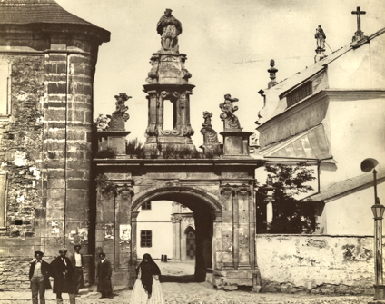 Archiwalna fotografia barokowej Bramy Katedralnej w Kamieńcu Podolskim, z rzeźbą św. Jana Nepomucena na szczycie. Przy bramie widoczna jest grupa przechodniów.