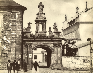 Archiwalna fotografia barokowej Bramy Katedralnej w Kamieńcu Podolskim, z rzeźbą św. Jana Nepomucena na szczycie. Przy bramie widoczna jest grupa przechodniów.