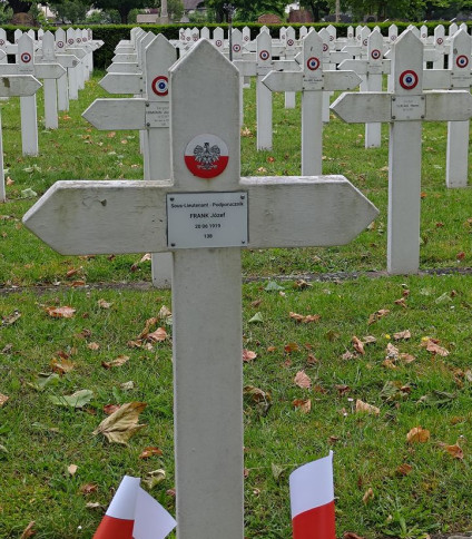 Biały krzyż z emblematem Polski i napisem 'Sous-Lieutenant - Podporucznik Frank Józef 20 06 1919 138' na Cmentarzu Zachodnim. Dwie małe polskie flagi z przodu.