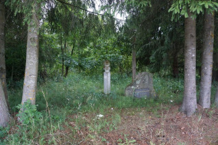 Cmentarz powstańców styczniowych otoczony drzewami. Widoczne są słup kapliczny, betonowy krzyż i głaz z litewską inskrypcją.