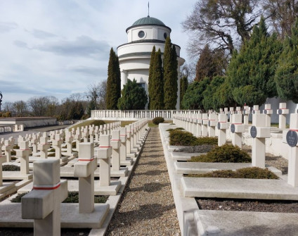 Widok na Cmentarz Orląt Lwowskich z rzędami białych krzyży i okrągłą kaplicą w tle, otoczoną drzewami.