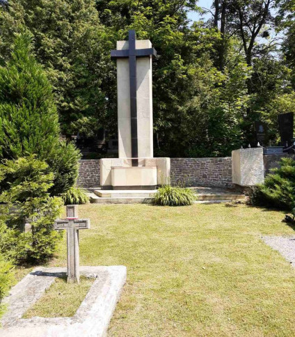 Centralny pomnik krzyża w kwaterze żołnierzy polskich na Cmentarzu Janowskim, otoczony zielenią i mniejszymi nagrobkami.