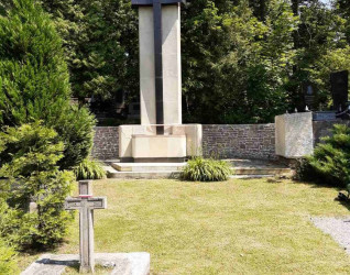 Centralny pomnik krzyża w kwaterze żołnierzy polskich na Cmentarzu Janowskim, otoczony zielenią i mniejszymi nagrobkami.