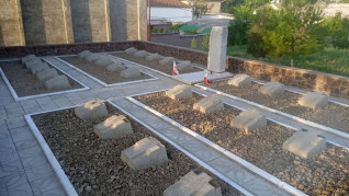 Polski cmentarz wojenny w Szachrisabz z rzędami symbolicznych mogił oznaczonych reliefami krzyża. W tle centralny pomnik z flagą, otoczony kamiennym murem.