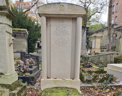 Nagrobek rodziny Szustermanów z cokolem schodkowym i aediculą z Gwiazdą Dawida. Inskrypcje widoczne na cokole, steli i płycie. Otoczony innymi grobami na cmentarzu.