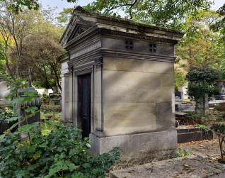 Kapliczka klasycystyczna z dwuspadowym dachem i tympanonem z wieńcem z szarfą. Boki ujęte pilastrami z głowicami, wejście zamknięte żeliwnymi drzwiami z ażurową górną częścią. Widoczne inskrypcje nad wejściem.