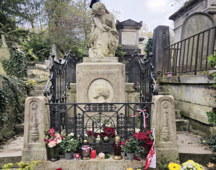 Grób Fryderyka Chopina z rzeźbą siedzącej muzy trzymającej lirę. Grób otoczony ozdobną kratą i kwiatami. Na postumencie owalny medalion z profilem Chopina.