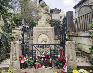 Grób Fryderyka Chopina z rzeźbą siedzącej muzy trzymającej lirę. Grób otoczony ozdobną kratą i kwiatami. Na postumencie owalny medalion z profilem Chopina.