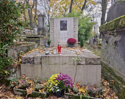 Grób Idalii i Miłosza Maginów z wysoką prostokątną stelą z brązową plakietą. Inskrypcje pod plakietą i na czole cokołu. Na grobie umieszczone są kwiaty i znicze.