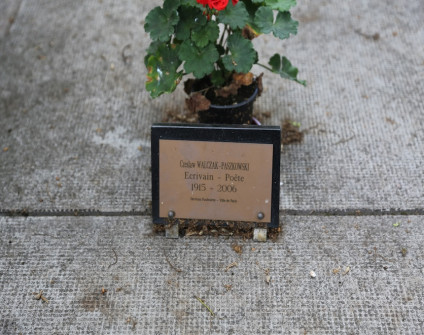 Płyta grobowa z metalową tabliczką z napisem 'Czesław Walczak-Paszkowski, Ecrivain - Poète, 1915-2006'. Za tabliczką stoi doniczka z czerwonymi kwiatami.