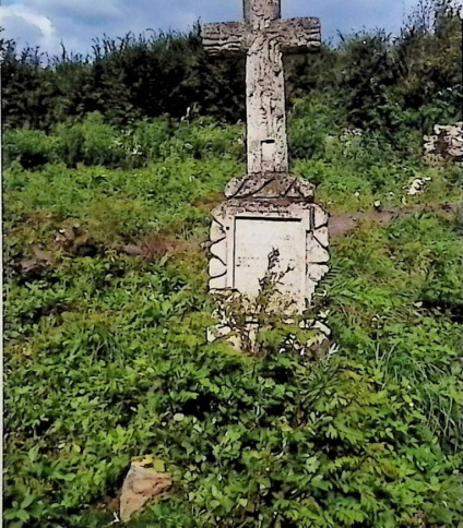 Grób oznaczony krzyżem stylizowanym na pień drzewa na cokole w formie skałek z kamienną podstawą. Krzyż zdobiony płaskorzeźbionymi liśćmi dębu. U dołu widoczne puste miejsce na fotografię.