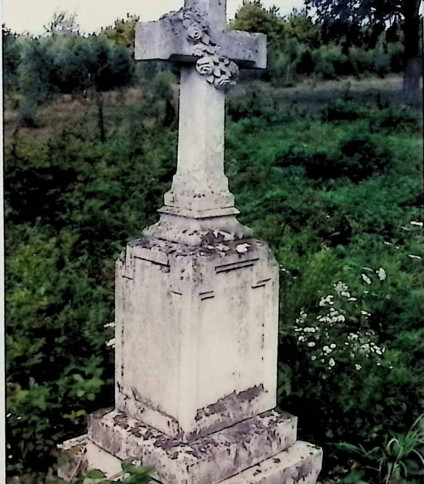 Nagrobek Praksedy Szkuby z krzyżem na cokole i dwustopniowej podstawie. Krzyż z wieńcem kwiatowym przewieszonym przez ramiona. Cokół z ściętymi krawędziami i małymi ostrosłupami w narożach.