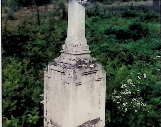 Nagrobek Praksedy Szkuby z krzyżem na cokole i dwustopniowej podstawie. Krzyż z wieńcem kwiatowym przewieszonym przez ramiona. Cokół z ściętymi krawędziami i małymi ostrosłupami w narożach.