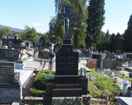 Nagrobek Anny Hanak, Filipa Hanaka i Heleny Kawulok z krzyżem na trójstopniowym cokole. Krzyż z figurą Chrystusa i napisem 'REX VIDE CREATOR'. Cokół z rytymi inskrypcjami, po bokach metalowe lampiony.