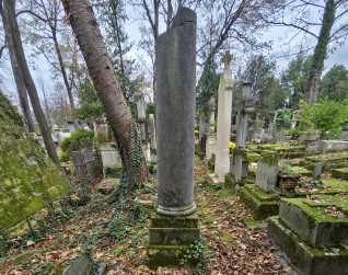 Miejsce pochówku z płaską płytą nagrobną na ziemi oraz ułamaną kolumną marmurową z bazą przy wezgłowiu, na postumencie. Widoczne drzewa i inne groby.