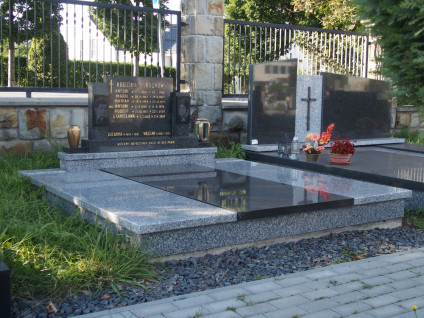 Nagrobek rodziny Płoszków z wysoką podstawą i stelą z krzyżem oraz inskrypcjami. Portrety mężczyzn wygrawerowane na bocznych tablicach. Na podstawie metalowy wazon i lampion.