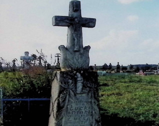 Nagrobek z krzyżem przypominającym pień drzewa na cokole w formie skał. Zawiera płaskorzeźbę Chrystusa i klęczącego anioła z motywami winorośli otaczającymi inskrypcję.