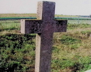 Kamienny krzyż oznaczający grób Andrzeja Winnickiego, z pionową płytą z wyrytym obramowaniem i inskrypcją, w otoczeniu trawiastego krajobrazu.