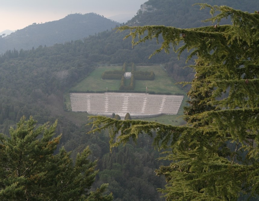 Vue du cimetière militaire polonais à Monte Cassino, entouré de verdure luxuriante et de collines. Le cimetière est en terrasses avec un monument central visible.