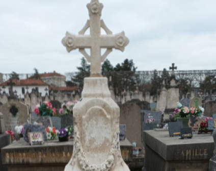 Wapienna stela zwieńczona krzyżem na grobie Stefana Paszkowicza w Roanne, Francja. Stela otoczona innymi grobami z kwiatami i tabliczkami.