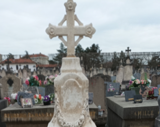 Wapienna stela zwieńczona krzyżem na grobie Stefana Paszkowicza w Roanne, Francja. Stela otoczona innymi grobami z kwiatami i tabliczkami.