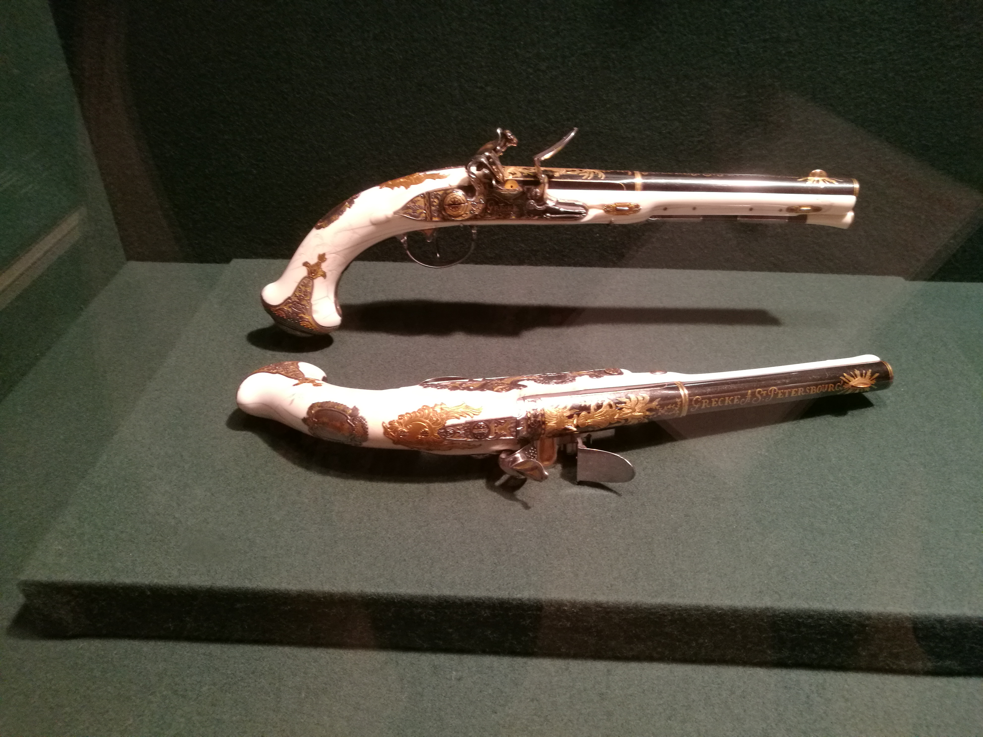 Deux pistolets à silex décorés avec des poignées blanches et des ornements dorés, présentés dans une vitrine de musée.