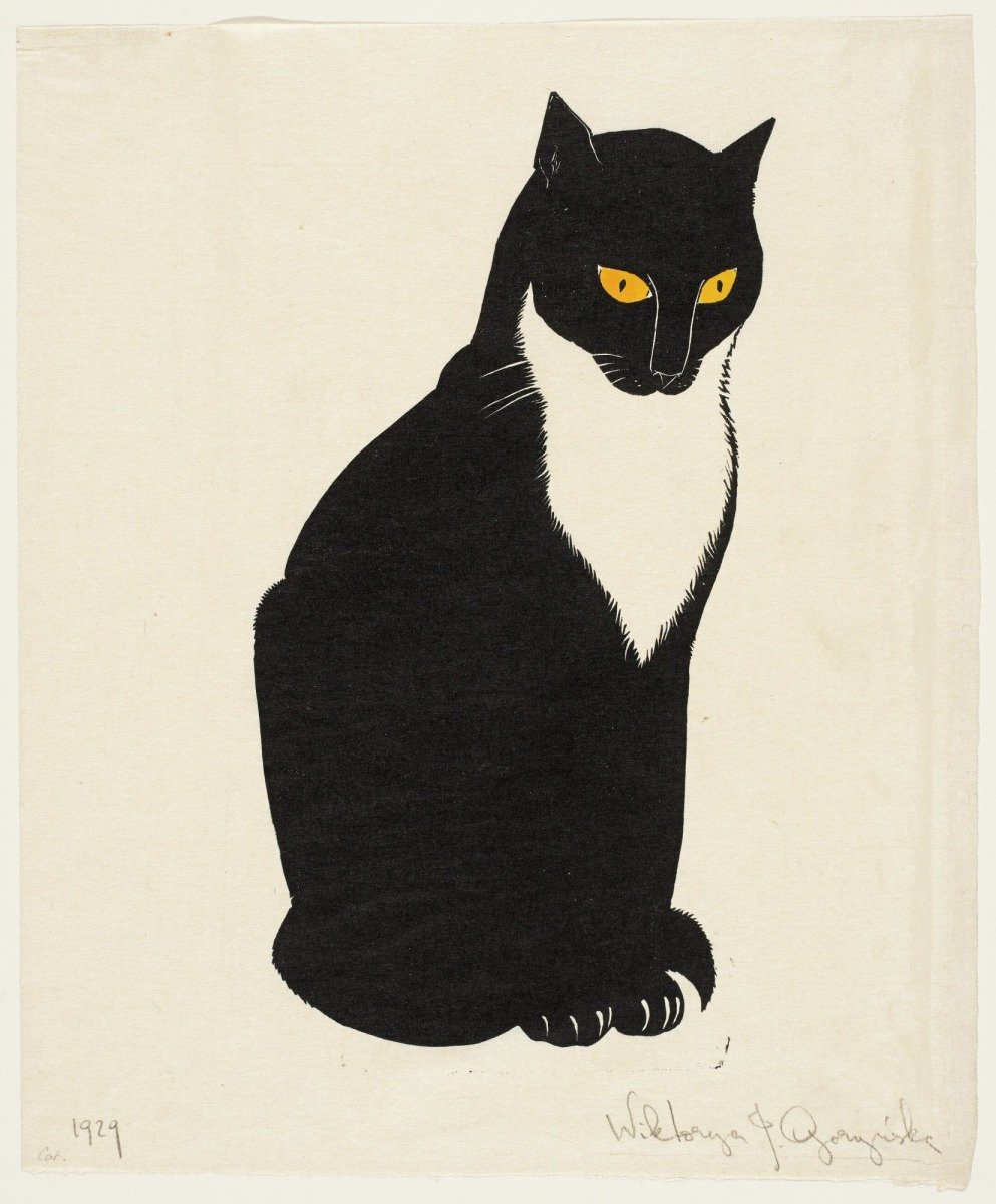 A black cat with yellow eyes and a white chest sits against a plain background. The artwork is a woodcut by Wiktorja J. Goryńska from 1929.