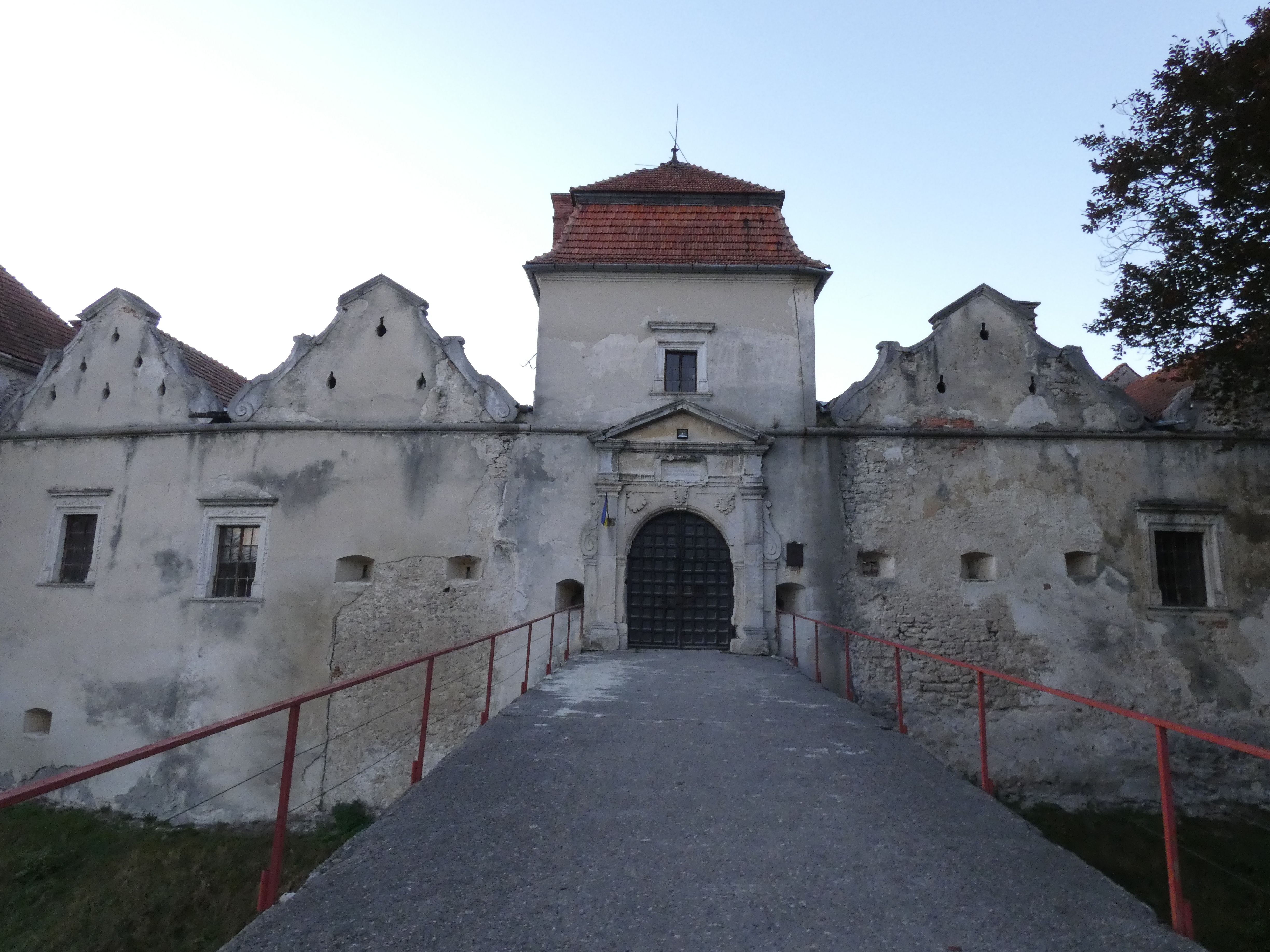 The entrance to Swirz castle with a stone portal and triangular abutment, flanked by decorative gables and a red tile roof. A bridge leads to the gate.