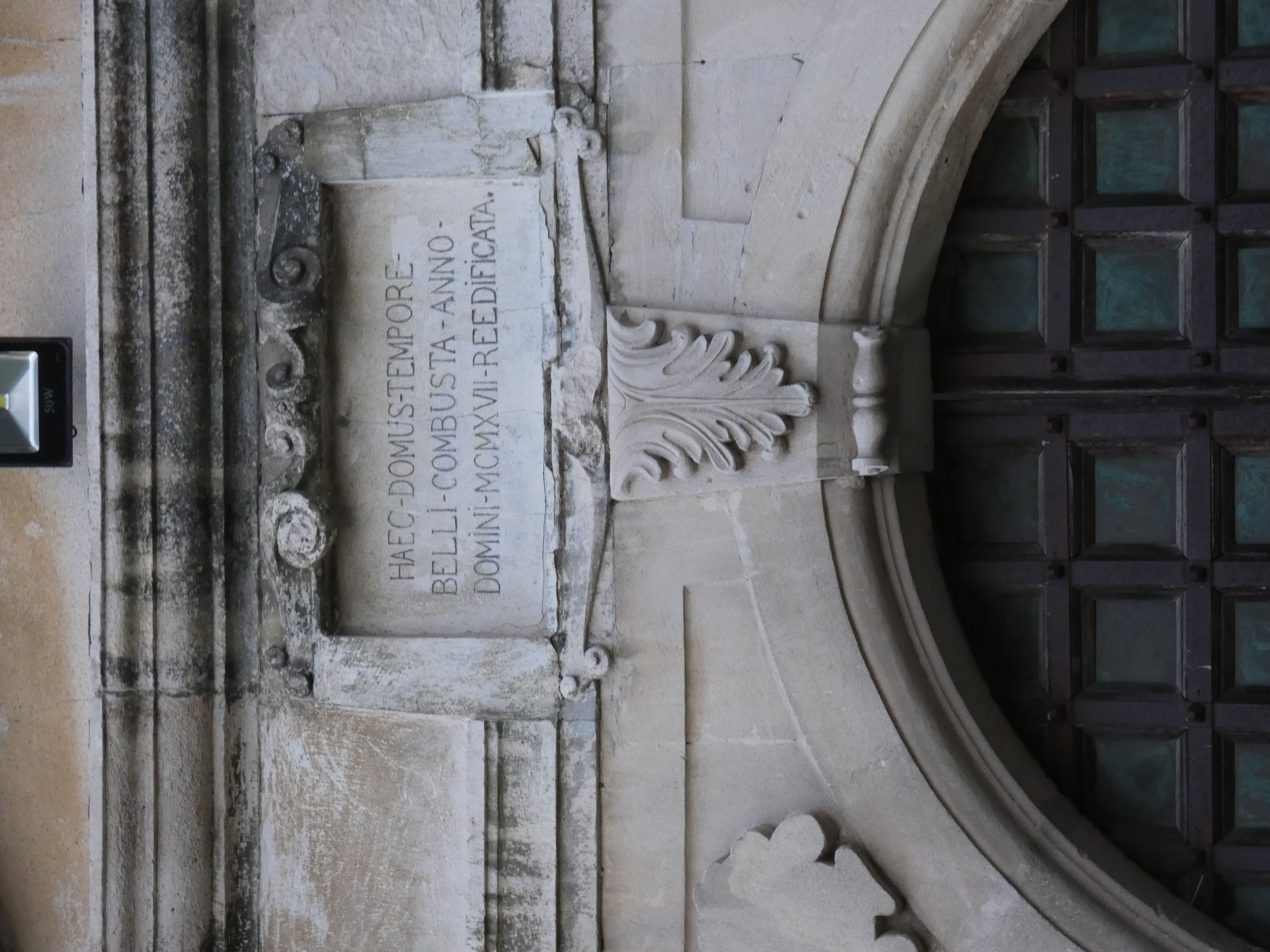 Stone inscription above the arched entrance in the castle at Swirz with Latin text: 'HAEC DOMUS TEMPORE BELLI COMBUSTA ANNO DOMINI MCMXVII REEDIFICATA.' The inscription is surrounded by decorative elements.