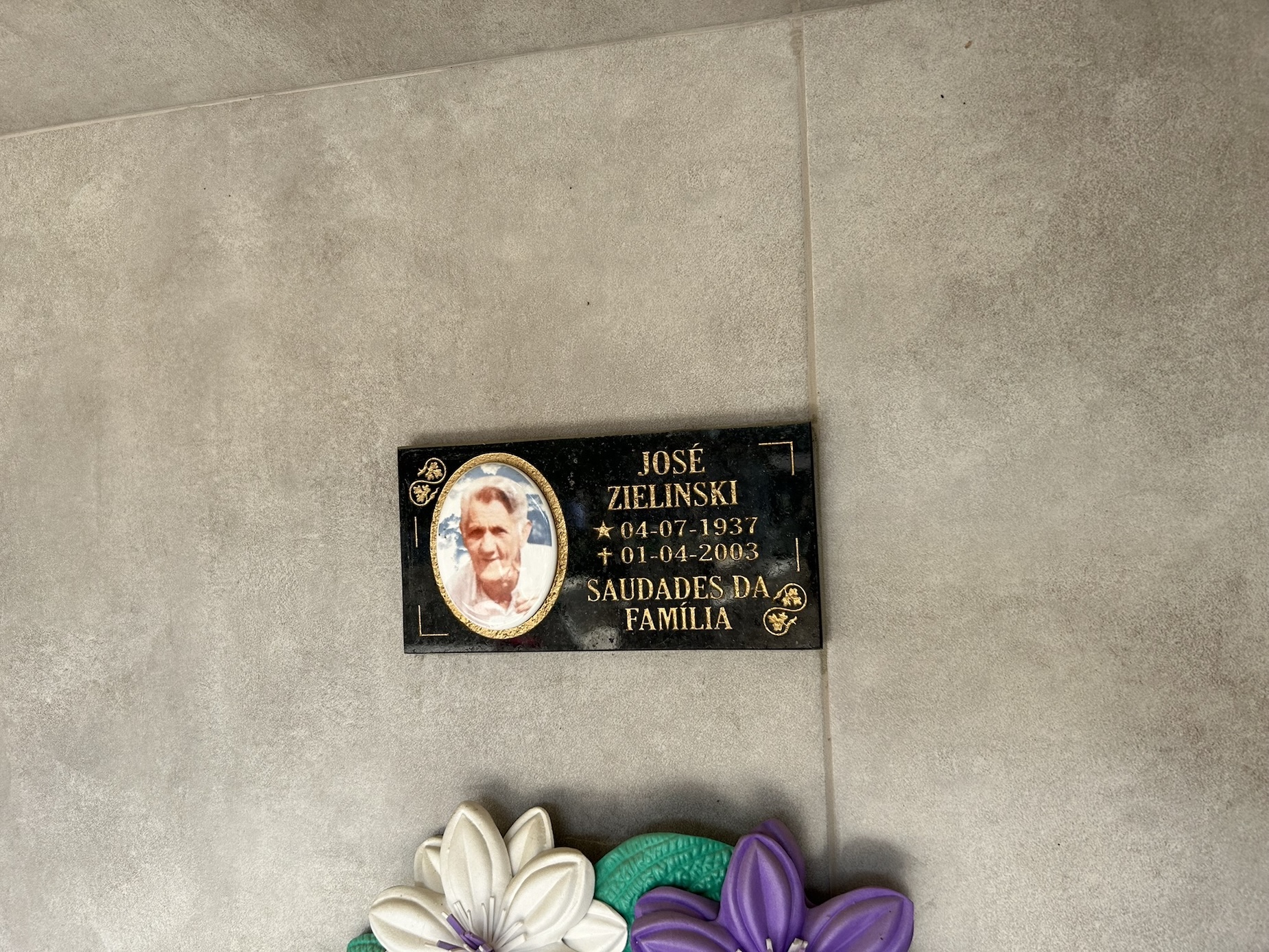 Plaque with photograph and inscription for Jozef Zielinski, born 04-07-1937, died 01-04-2003, with text 'Saudades da Familia'. Below decorative flowers.