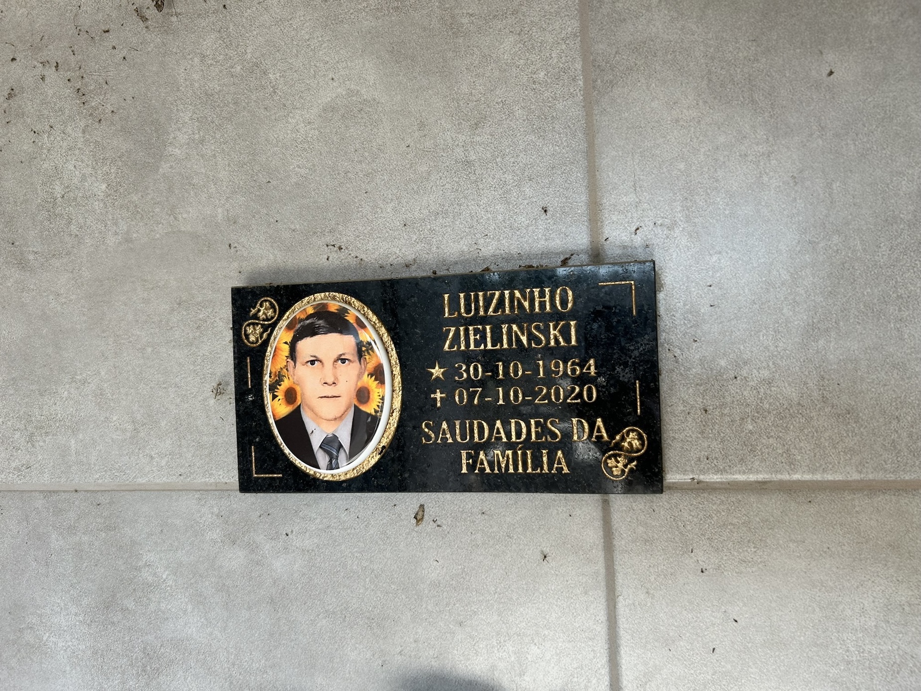 Memorial plaque with a photograph of a man surrounded by sunflowers. Text: 'Luizinho Zielinski, 30-10-1964, 07-10-2020, Saudades da Família.'
