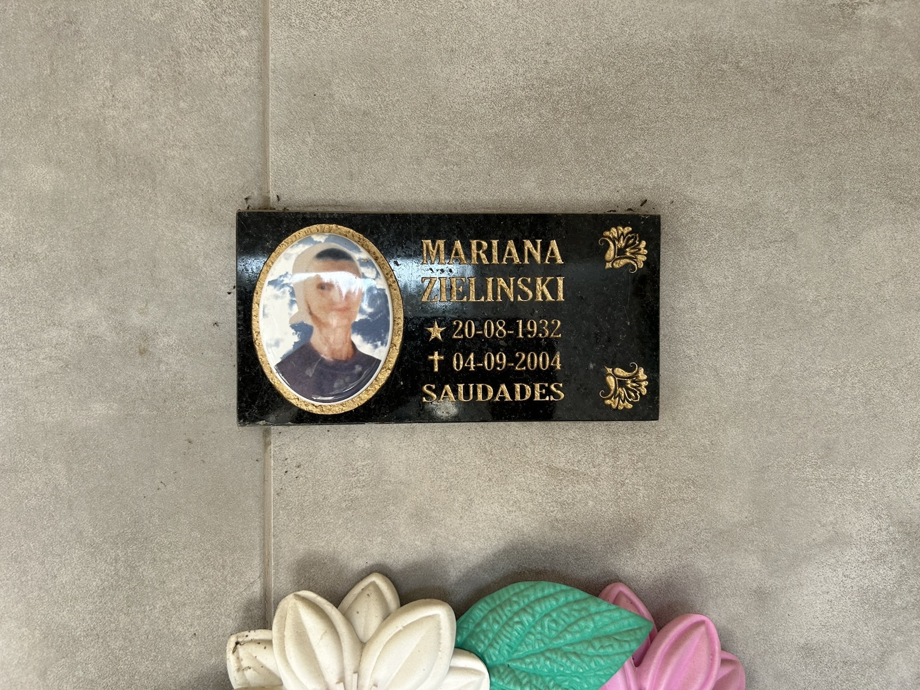 Plaque on gravestone with the name Marian Zielinski, date of birth 20-08-1932, date of death 04-09-2004 and the word 'Saudades'. Includes blurred portrait and decorative elements.