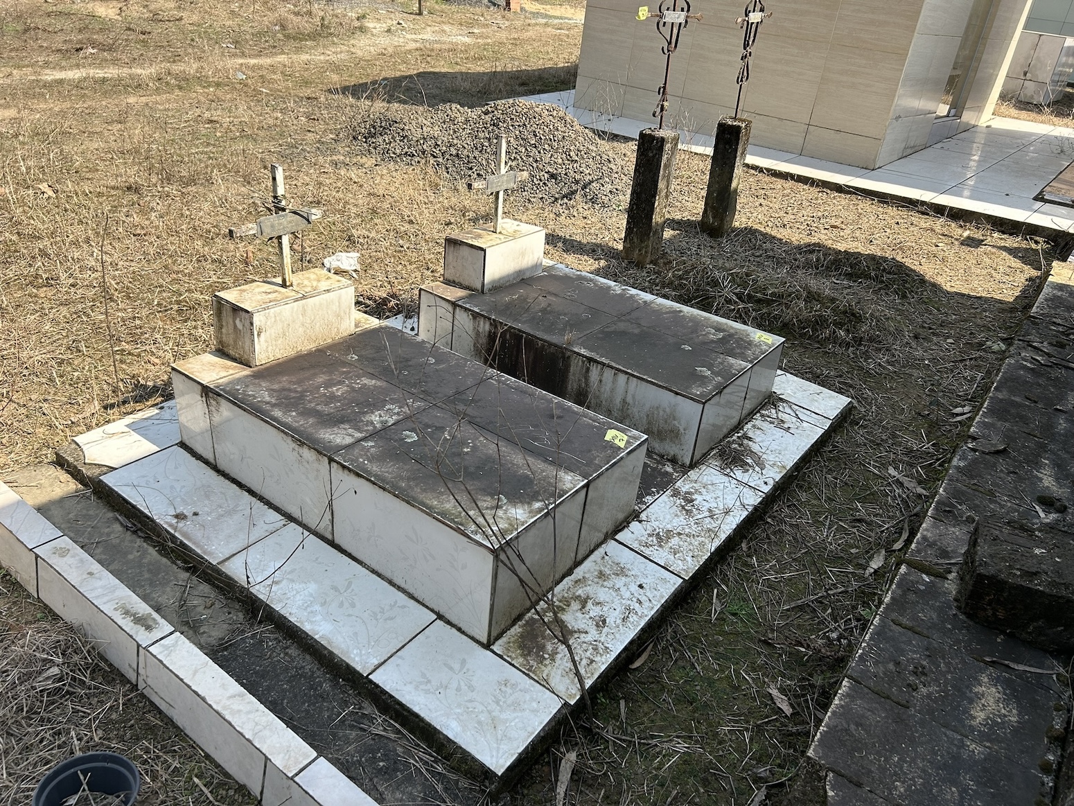 The grave of Regina and Zygmunt Michalski with two stone crosses on a tiled base, surrounded by dry grass.