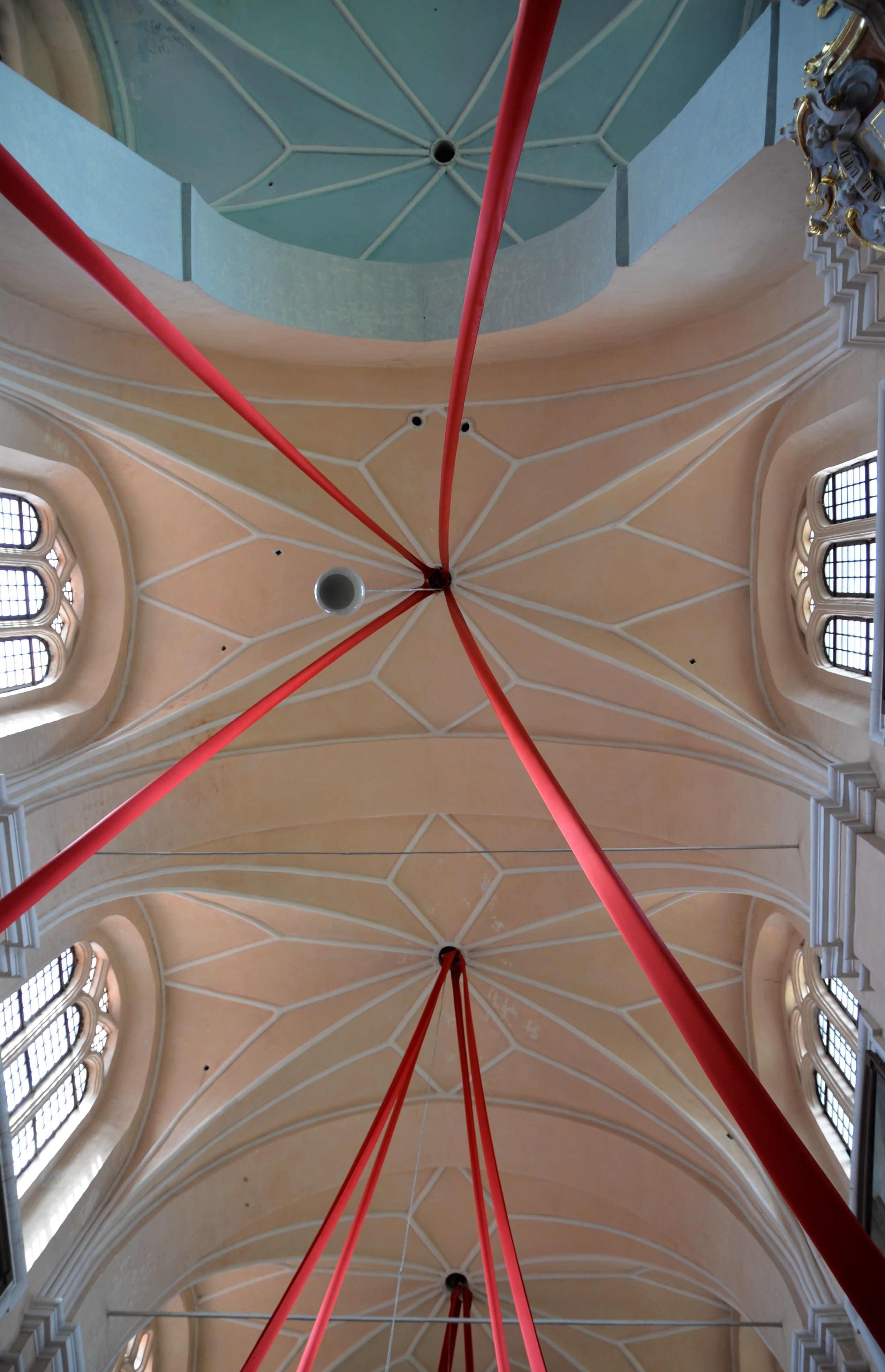 Interior of the Bernardine church in Cytowiany, showing a vaulted ceiling with red ribbons extending from a central point. The ceiling features geometric patterns and arched windows.