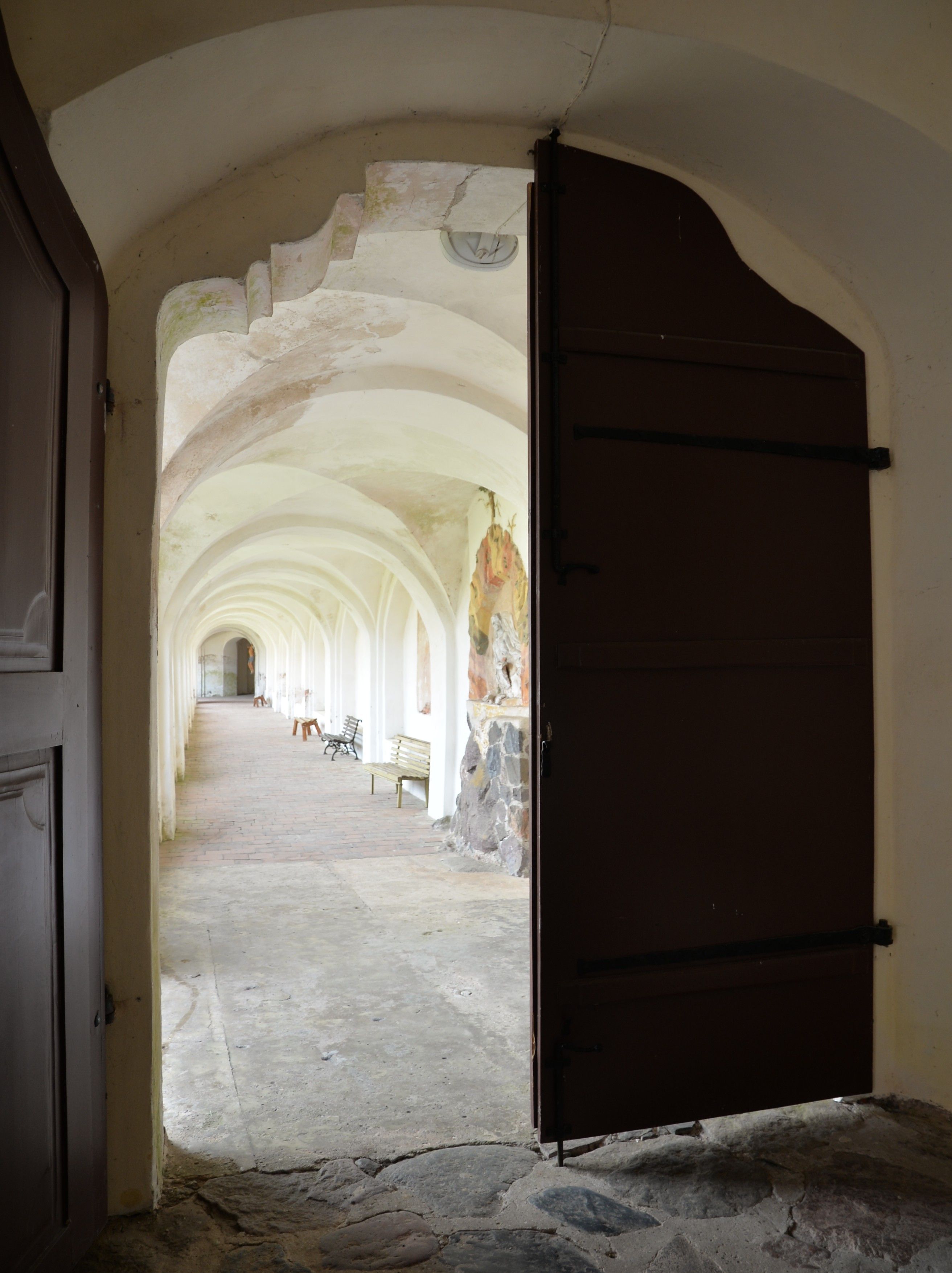 View through an open door into a corridor with arched ceilings and benches along the walls. The corridor is part of the Bernardine monastery complex in Cytowiany.