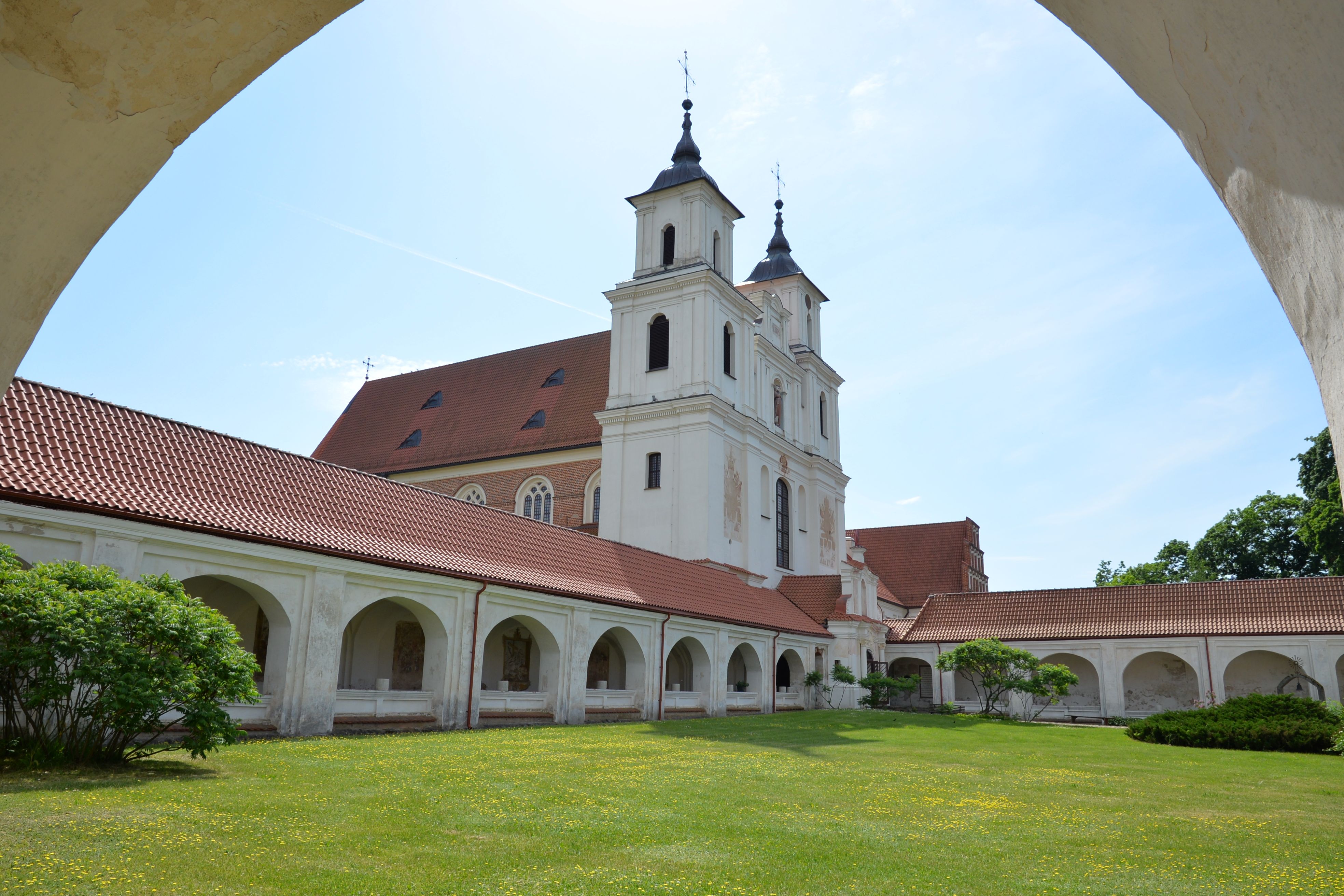 The Bernardine church and monastery in Cytowiany, featuring two towers and surrounded by cloisters with arches. The courtyard is grassy with small shrubs.