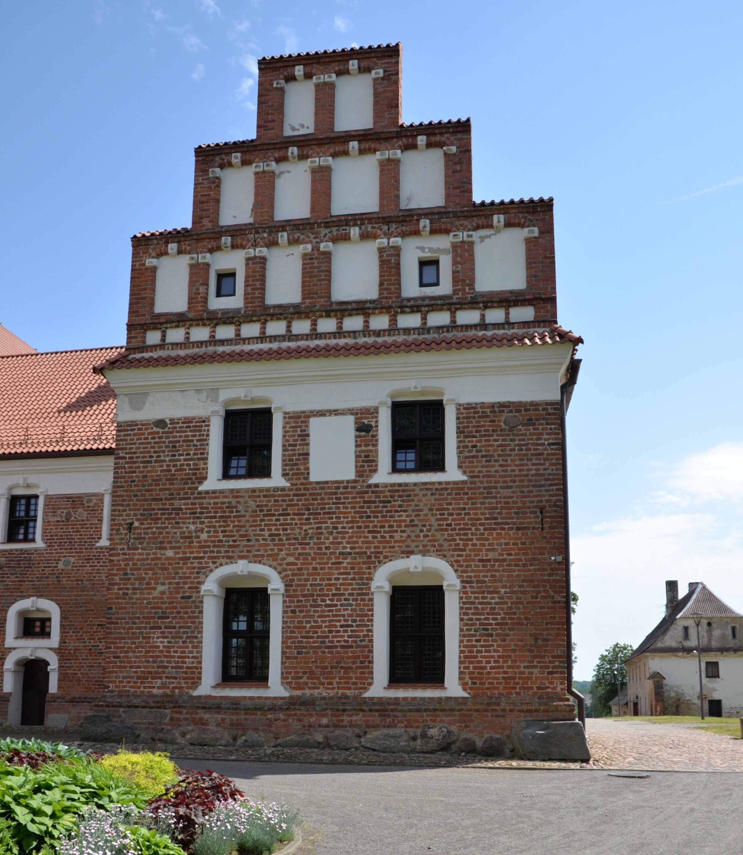 Brick building with a stepped gable and arched windows, part of the Bernardine church and monastery complex in Cytowiany. The structure features a red tiled roof and decorative white elements.