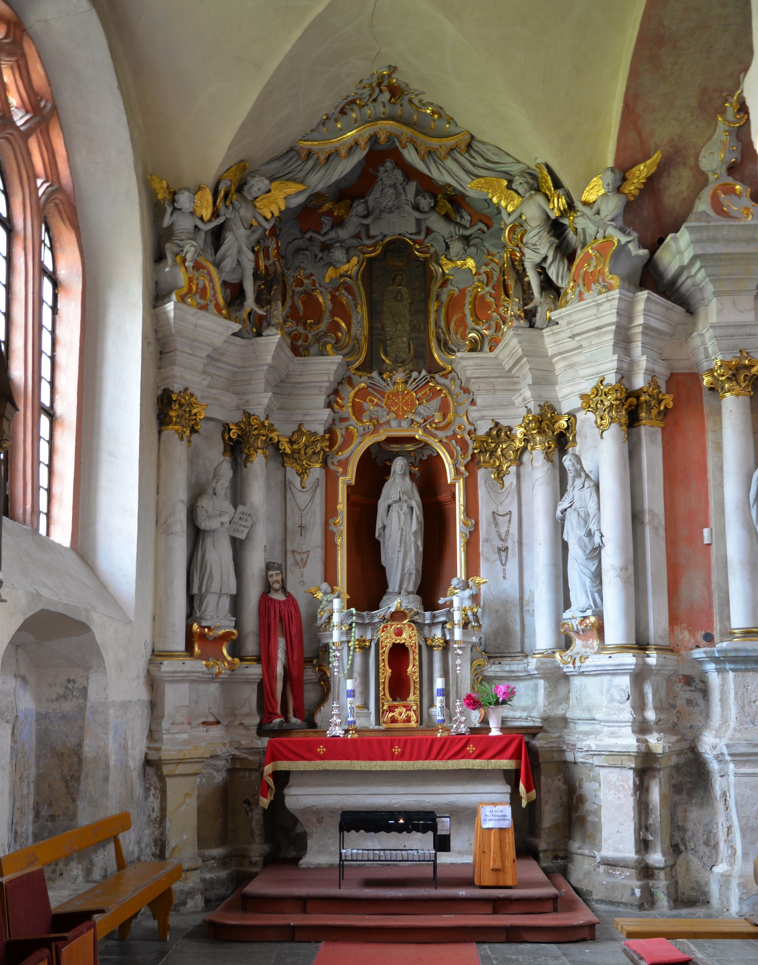 Baroque altar with a statue of the Virgin Mary, surrounded by angels and decorative elements, in the Bernardine church in Cytowiany. Red cloth covers the altar, with candles and flowers placed on it.