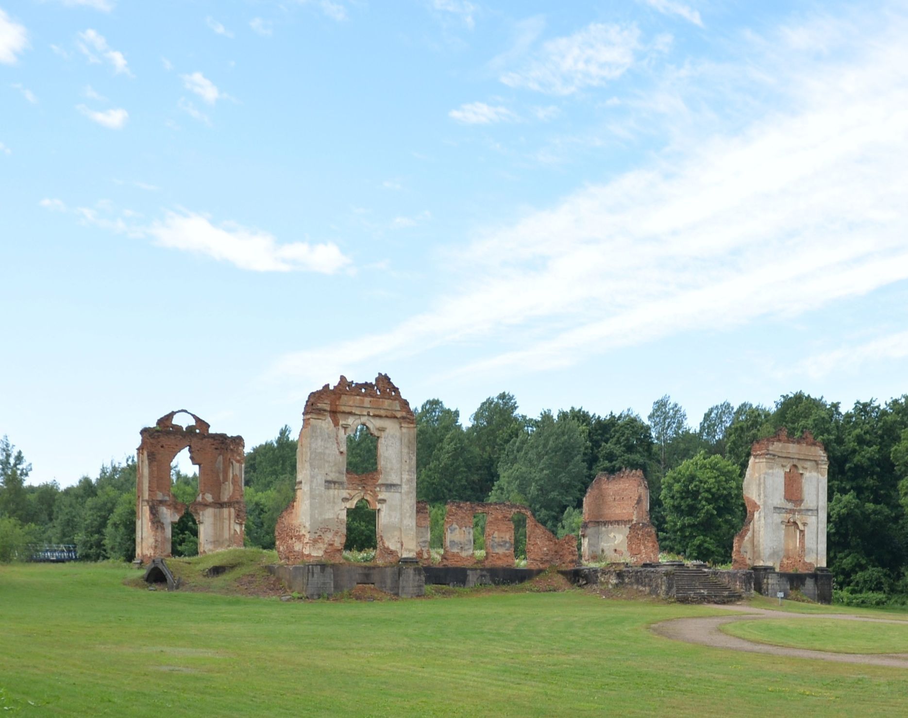 Ruins of the palace complex in Pawłów, with remnants of brick walls and arches, surrounded by greenery and a clear sky.