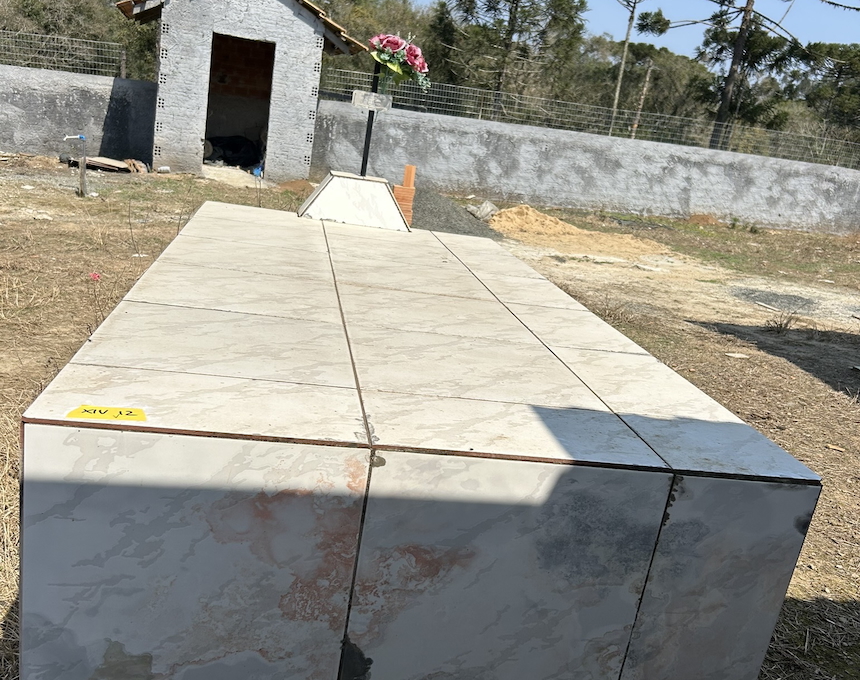 Marble gravestone of Irena Zielinska with a small cross and artificial flowers. A stone structure is visible in the background.