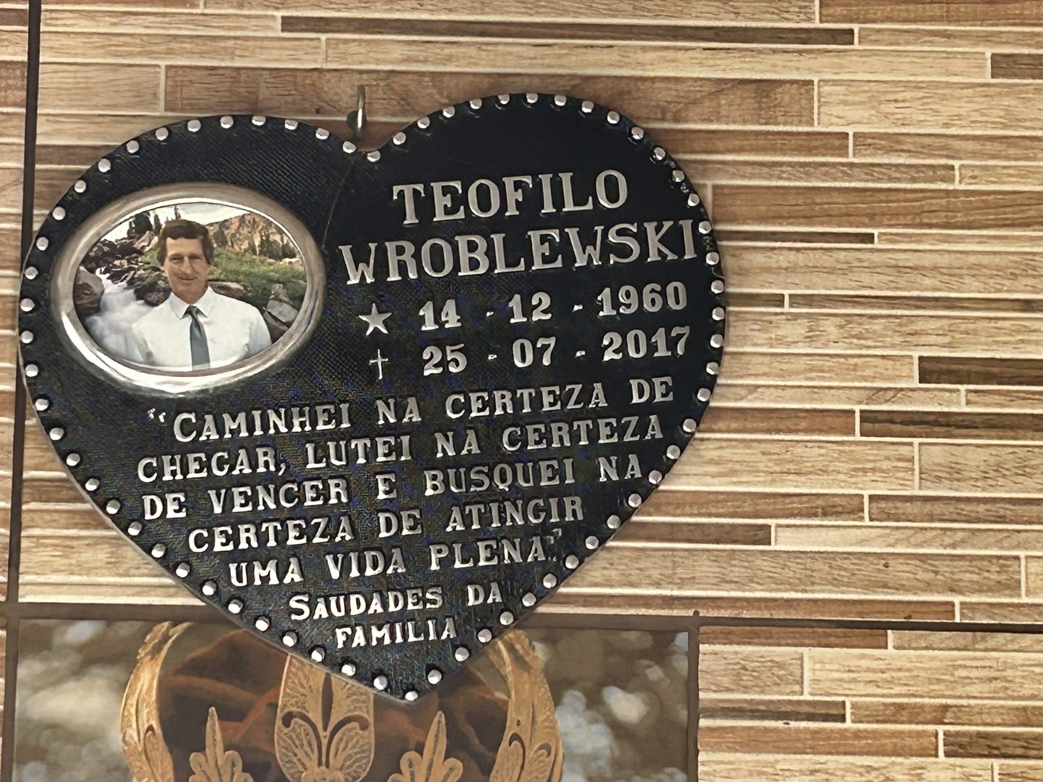 Heart-shaped plaque with a photograph of a man in a suit and text in Portuguese, including the name Teofilo Wroblewski and the dates 14-12-1960 and 25-07-2017, on a tile background.