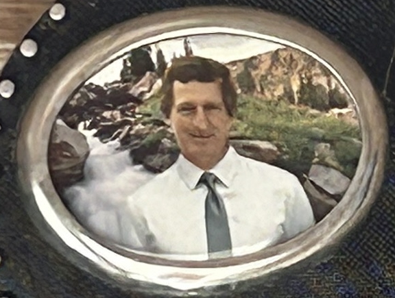 Portrait of a man in a white shirt and tie against a mountainous landscape with a waterfall.