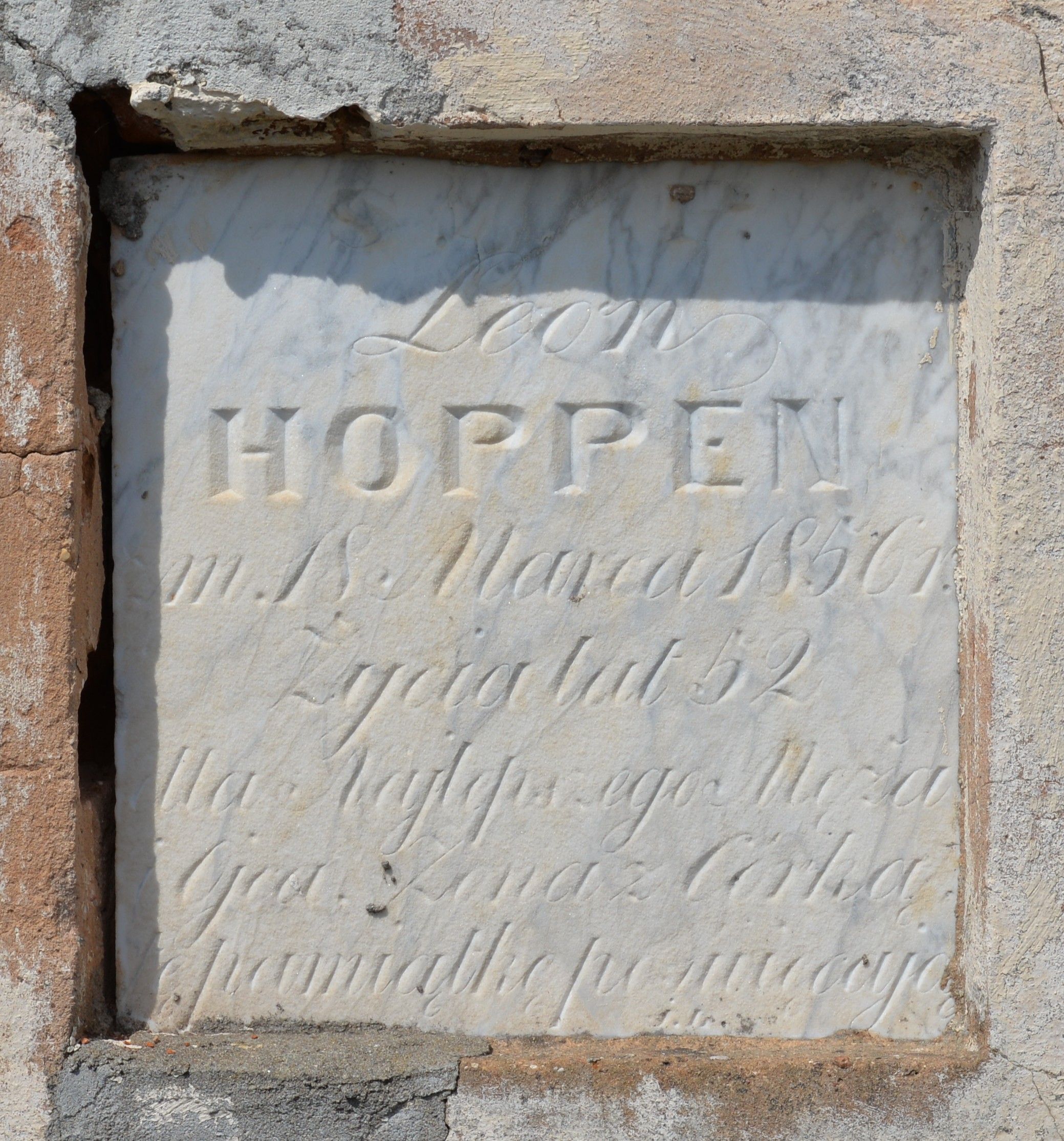 Marble epitaph plaque for Leon Hoppen on a tombstone, dated March 18, 1856, aged 52, with partially visible inscription in Polish, set in a weathered stone frame.