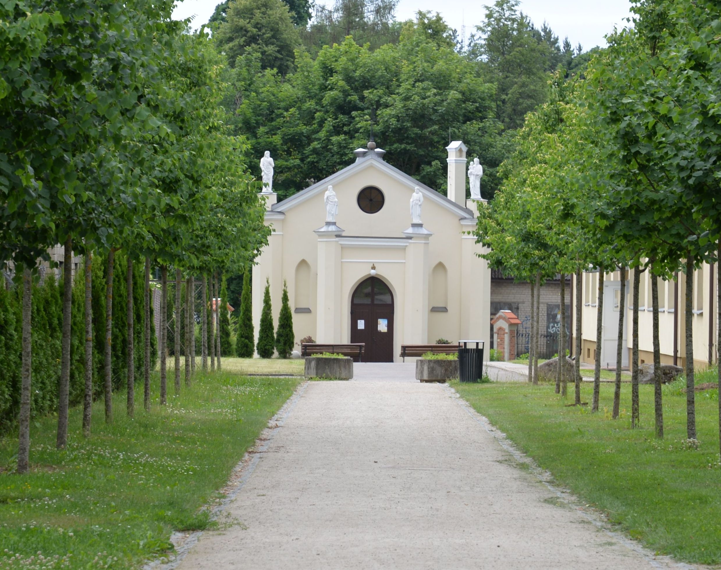 Une chapelle néogothique à Waka Trocka, entourée d'arbres avec un chemin menant à son entrée. Des statues ornent le toit, et le bâtiment est entouré de verdure.