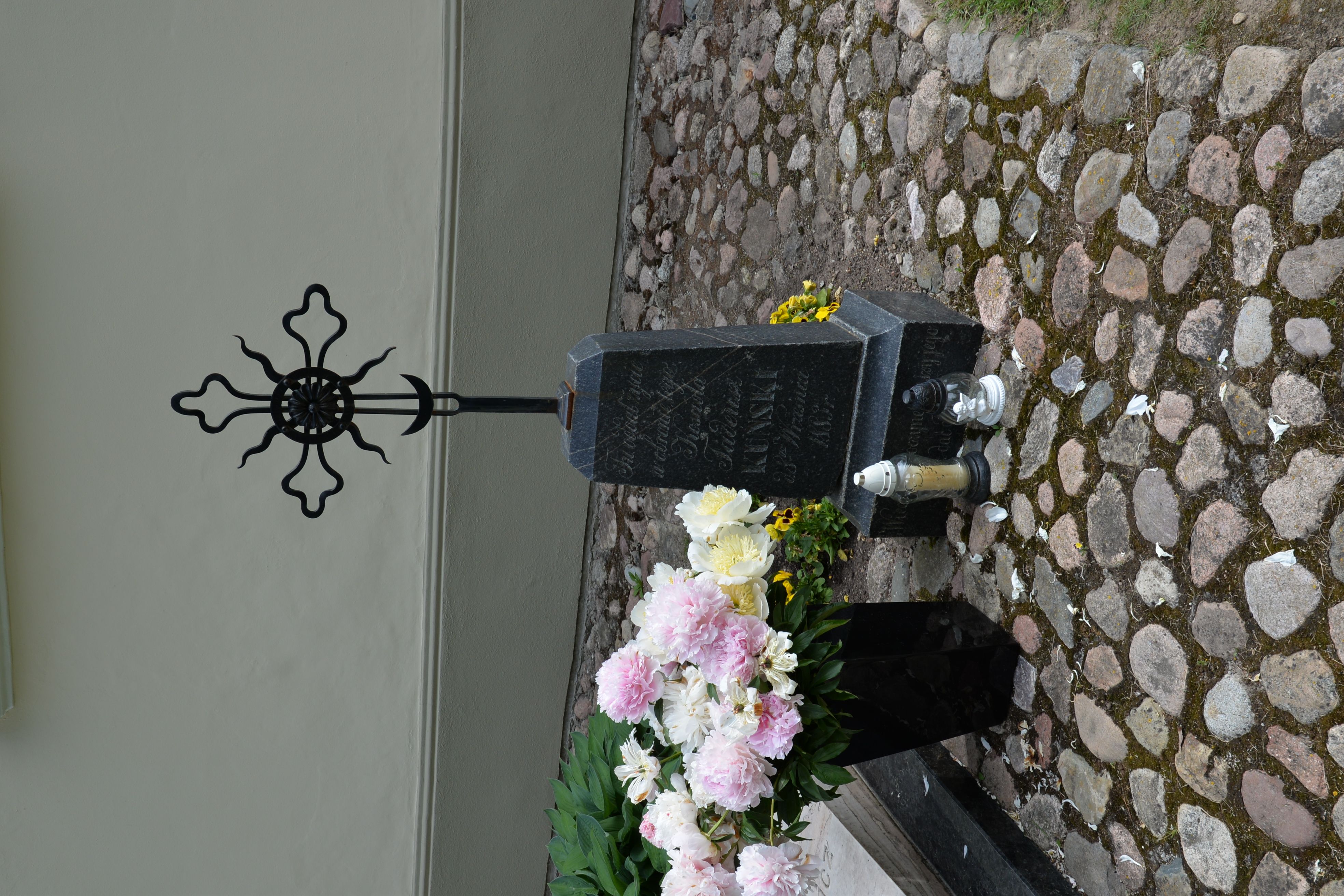 Tombe de Tadeusz Kuński avec une croix en fer sur une base en pierre, entourée de fleurs et de bougies, située près de la chapelle à Waka Trocka.