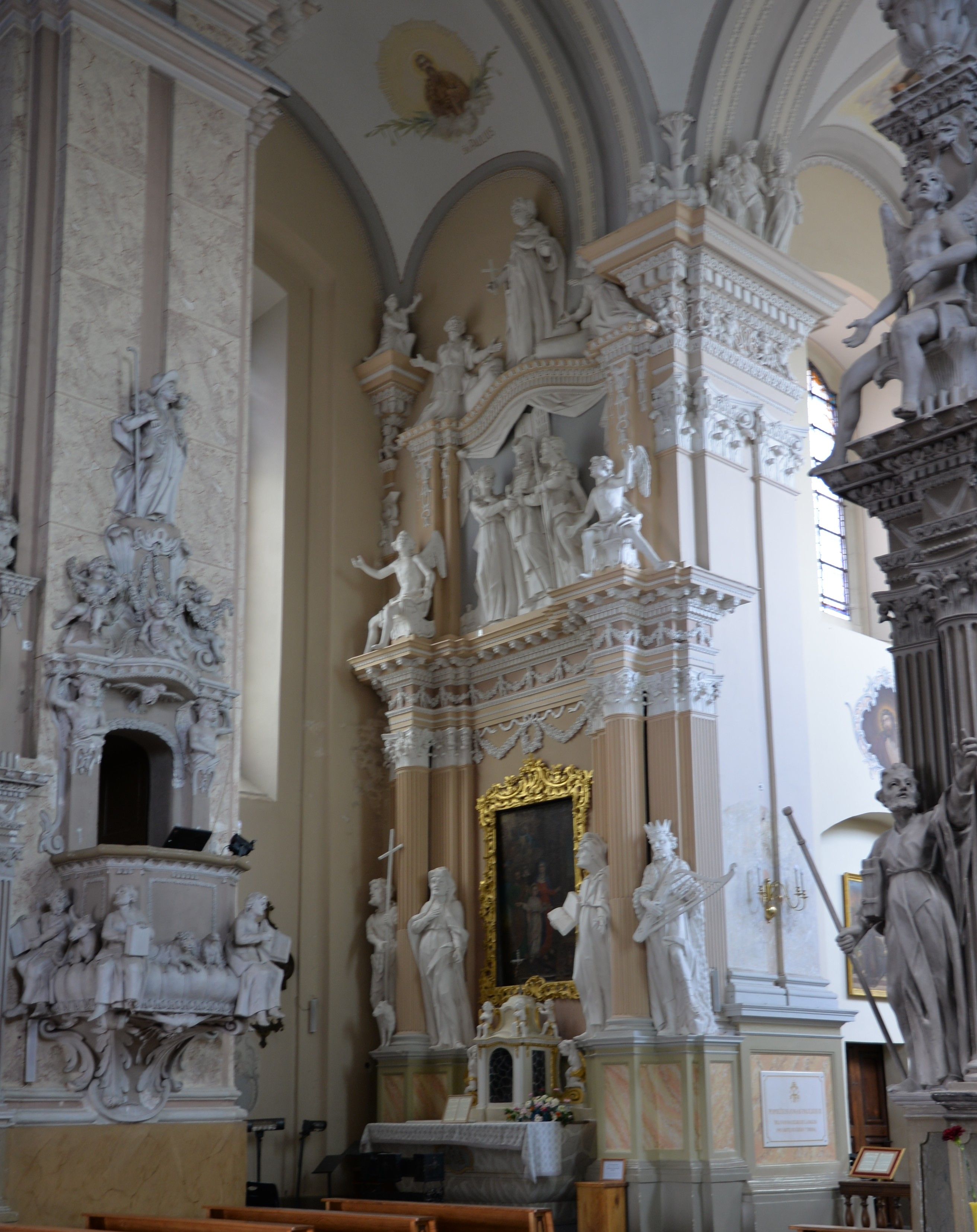 Intérieur de l'église de la Visitation de la Bienheureuse Vierge Marie à Szydłów, montrant un autel richement décoré avec des statues de saints et une peinture dans un cadre doré. L'architecture présente des éléments classiques et baroques.
