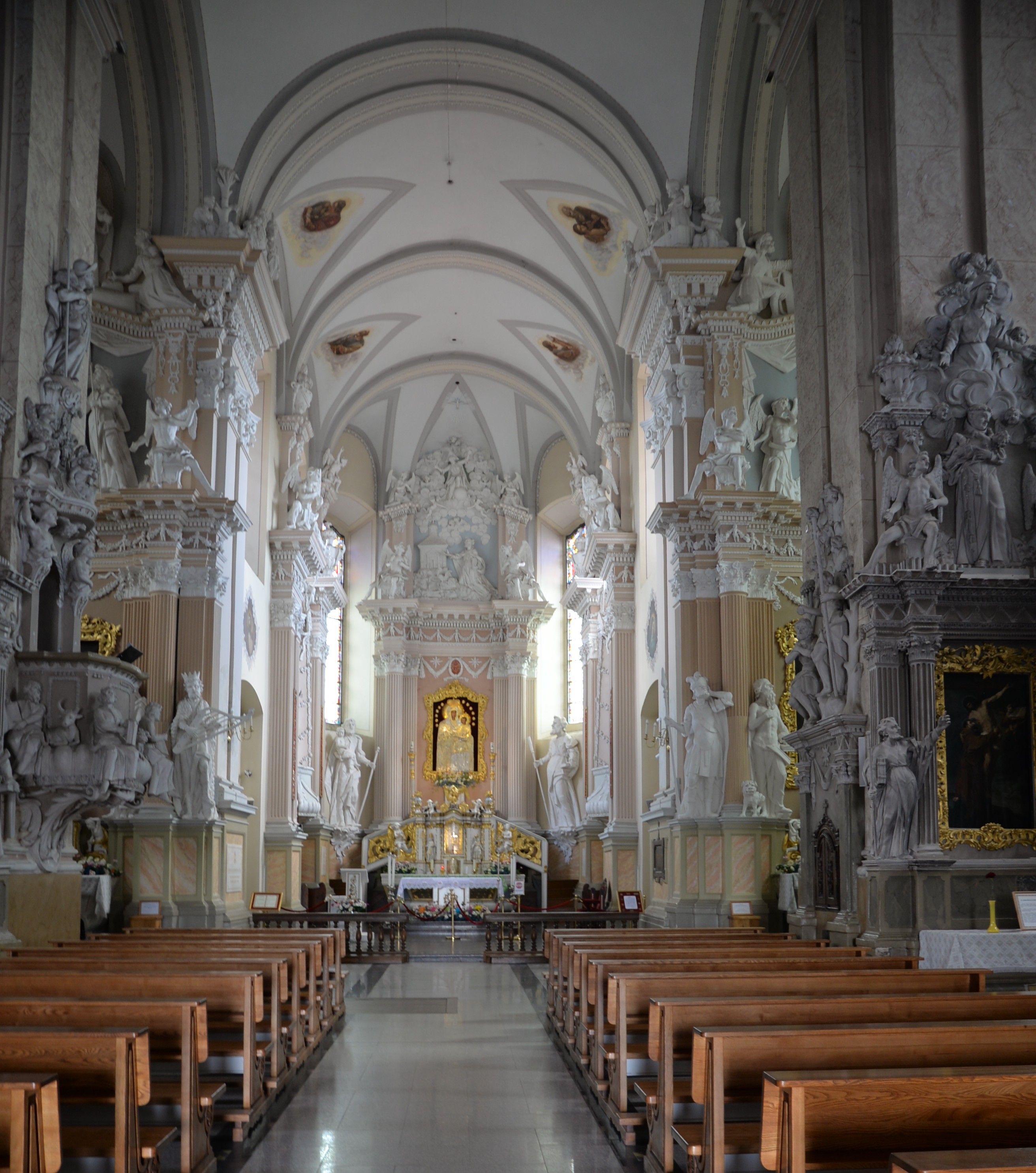 Intérieur de l'église de la Visitation de la Bienheureuse Vierge Marie à Szydłów, avec un autel richement décoré de sculptures et de peintures, entouré de colonnes ornées et de bancs.
